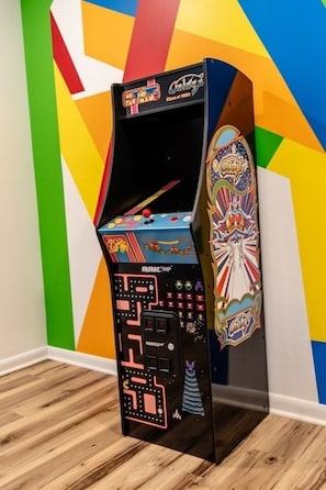A retro arcade machine with a colorful geometric wall in the background. - 5BR Mass Resort | Movie Lounge +Pool/Poker Table+Arcade+Gym+Remote Workstatio... (McGaheysville)