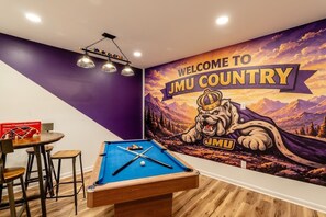 Een kamer met een pooltafel, een verwelkomend muurschildering en een barhoek.