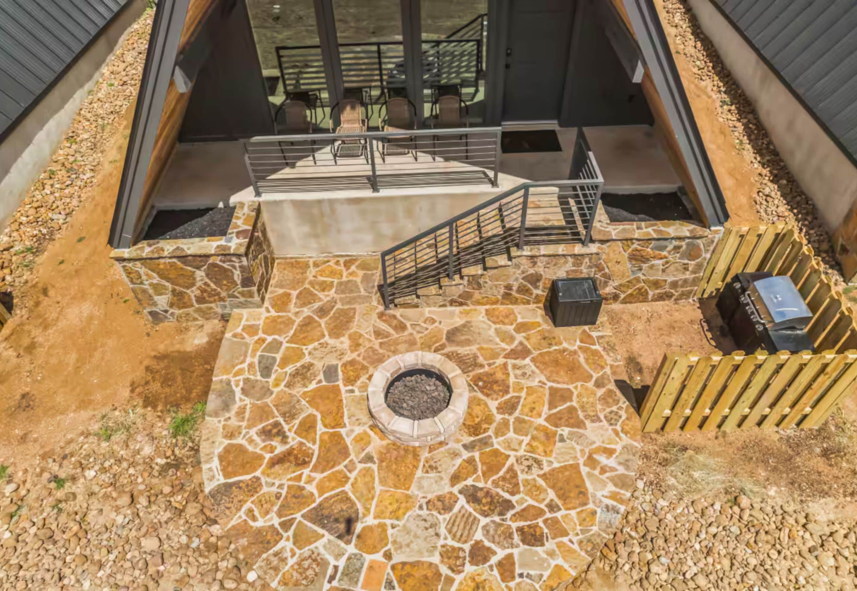 A stone patio with a fire pit, outdoor seating, and a staircase leading to an upper level.