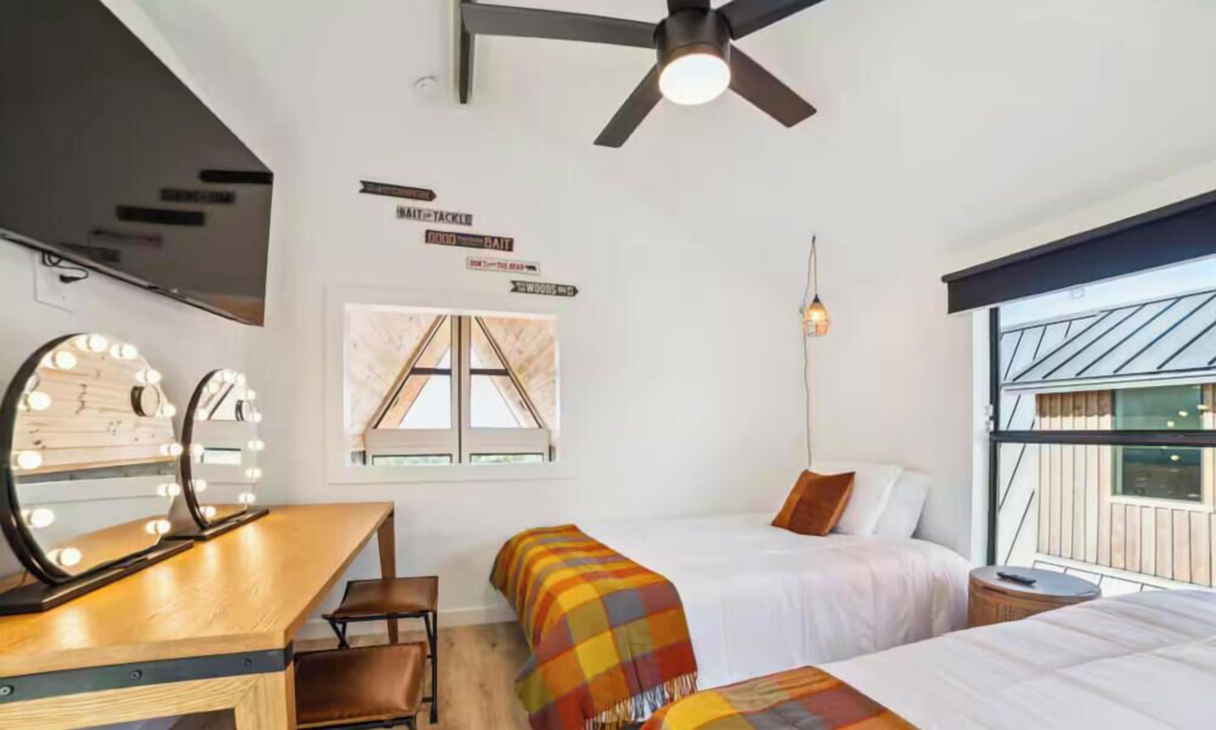 Quarto de hotel com cama, escrivaninha com espelho e ventilador de teto.