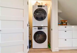 A laundry room with two stacked washing machines, a drying rack, and a storage cabinet with a camping book. - A-Frame Cabin | Community Ponds | Fire Pit (New Braunfels)