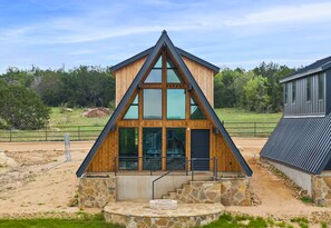 A modern building with a triangular roof, large windows, and a stone foundation. - 3 Side by Side A-Frame Cabins | Sleeps 24 | Ponds (New Braunfels)