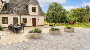 Une maison à deux étages avec un toit en tuiles, une terrasse avec des meubles d’extérieur et une allée gravillonnée.
