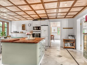 Une cuisine dotée d’un îlot central, d’un plafond en bois et donnant sur la salle à manger.