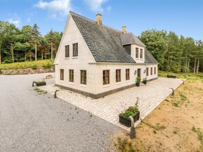 Une maison à deux étages avec une façade en pierre, de nombreuses fenêtres et une allée pavée.
