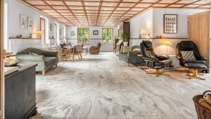 Un vaste espace de vie doté d’un plafond haut, de poutres en bois et d’un sol en marbre. On y trouve différents types de sièges, notamment des canapés et des fauteuils.