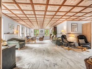 Ein großzügiger Wohnbereich mit hoher Decke, Holzbalken und Marmorboden. Es gibt verschiedene Sitzgelegenheiten, darunter Sofas und Sessel.