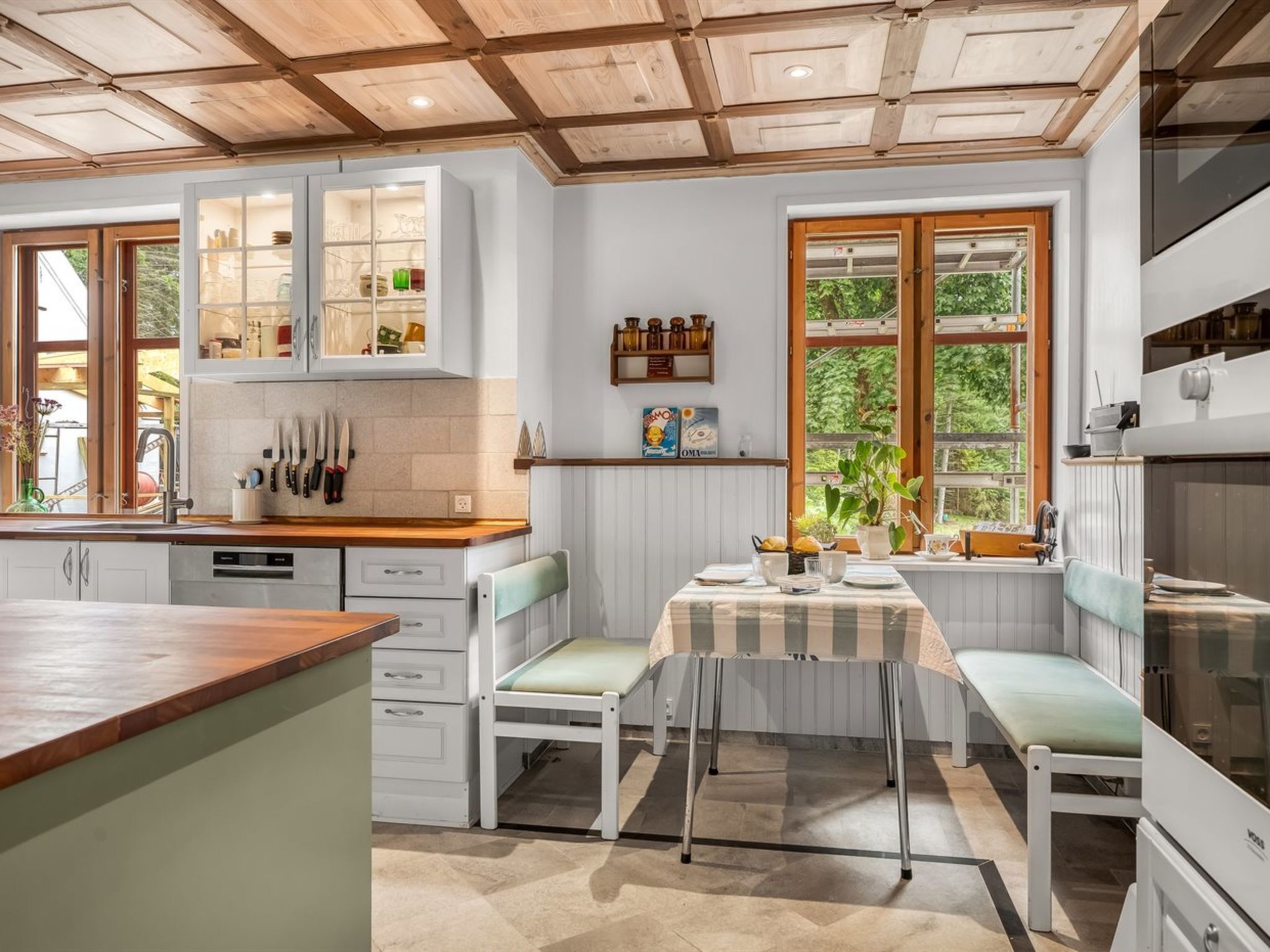 Una cocina con muebles blancos, encimera de madera y comedor con banco y mesa.