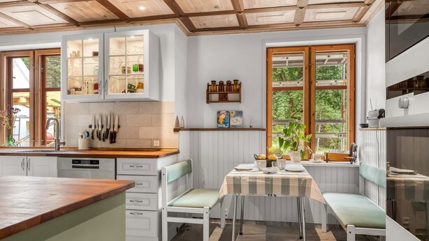 Une cuisine avec des meubles blancs, un plan de travail en bois et un coin repas comprenant un banc et une table.