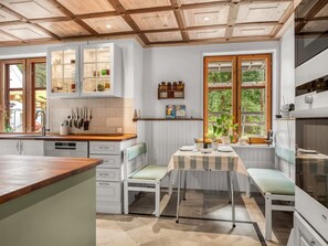 Uma cozinha com armários brancos, bancada de madeira e um espaço de refeições com banco e mesa.