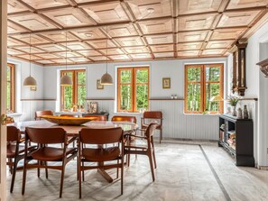 A dining area with a wooden table and chairs, large windows with views of greenery, pendant lighting, and a built-in bookshelf. - "Ajna" - 20.9km from the sea by Interhome (Jerslev J)