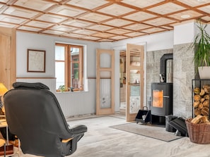 Ein gemütliches Wohnzimmer mit Kamin, einem bequemen Sessel und einer Holzbalkendecke.