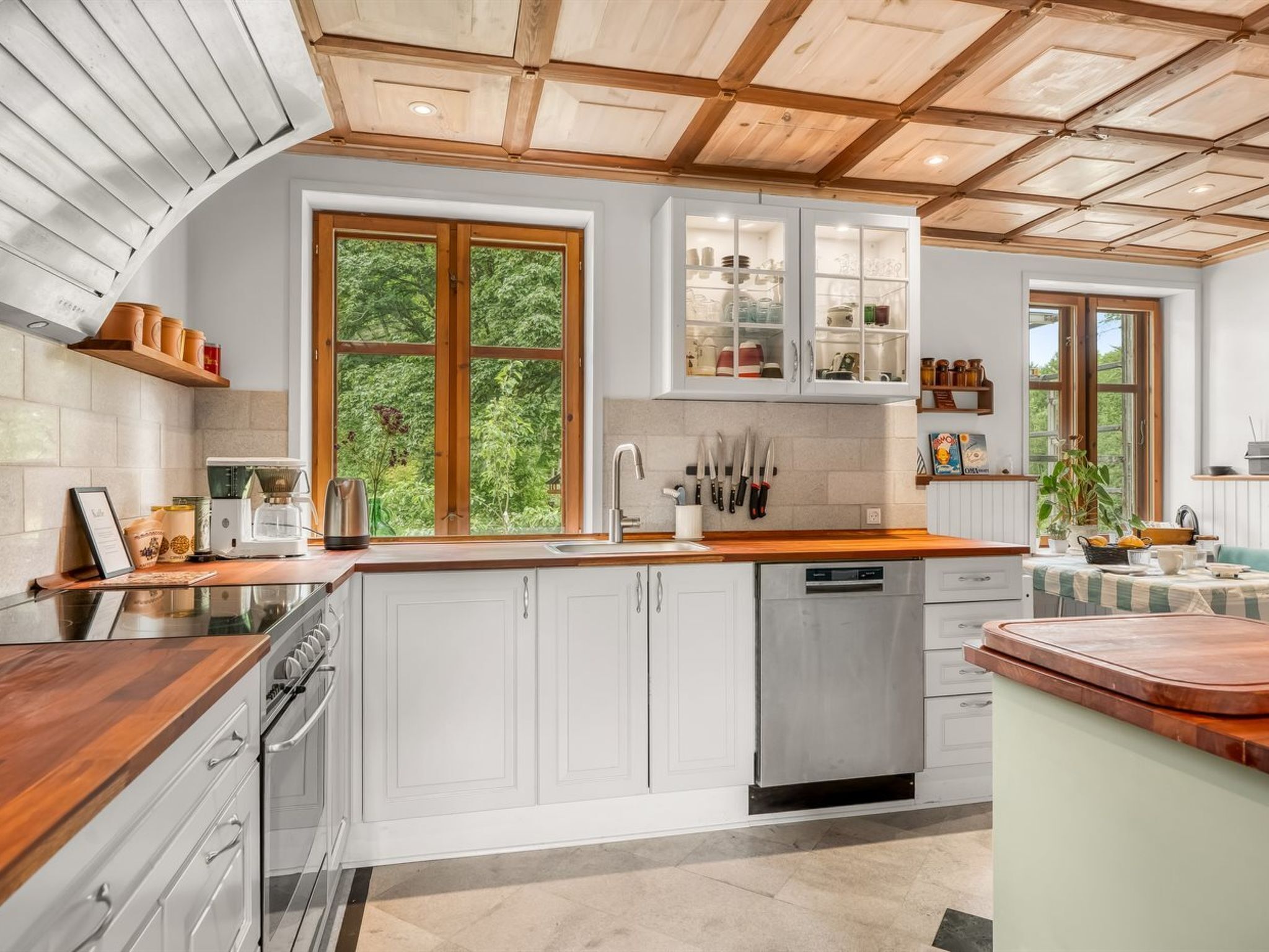 A modern kitchen with white cabinetry, a wooden countertop, and a view of greenery outside.