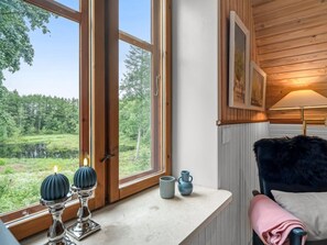 A room with a large window, a wooden ceiling, a lamp, a chair, and a table with decorative items. - "Ajna" - 20.9km from the sea by Interhome (Jerslev J)