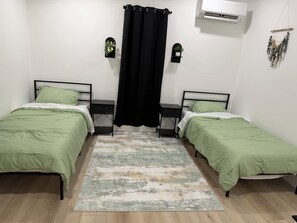 A room with two beds, a black curtain, an air conditioner, and two wall-mounted plants.