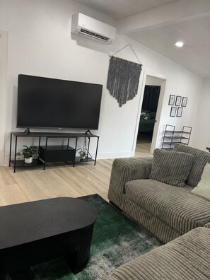 A modern living room with a flat-screen TV, a black coffee table, a striped sofa, and a hanging wall decoration.