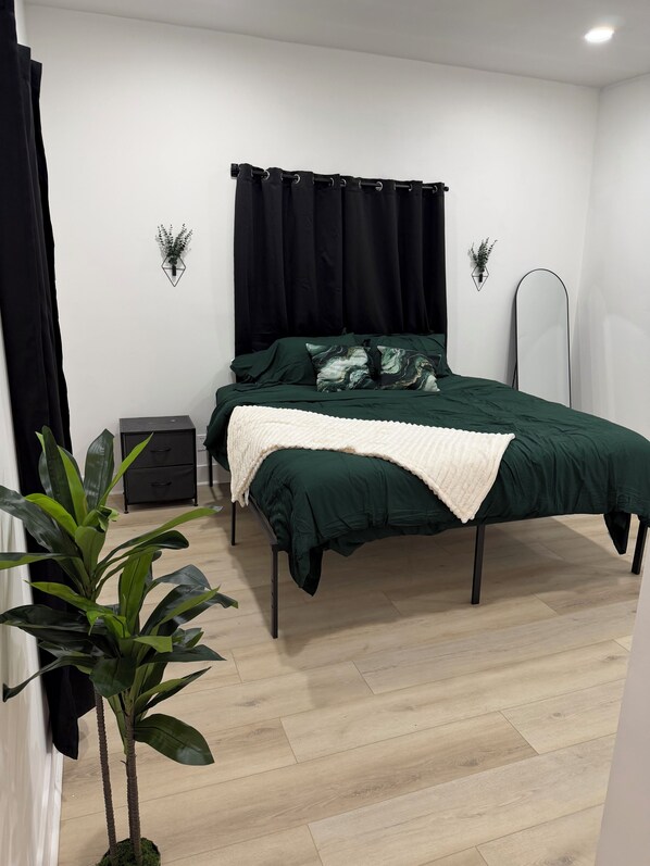 A bedroom with a bed, a bedside table, a mirror, and a potted plant.