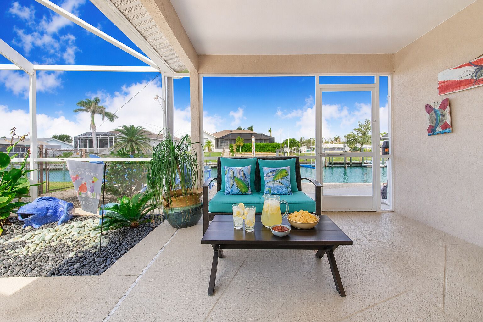 Un balcon spacieux donnant sur une piscine, une table avec des boissons et des en-cas, et un canapé turquoise agrémenté de coussins décoratifs.