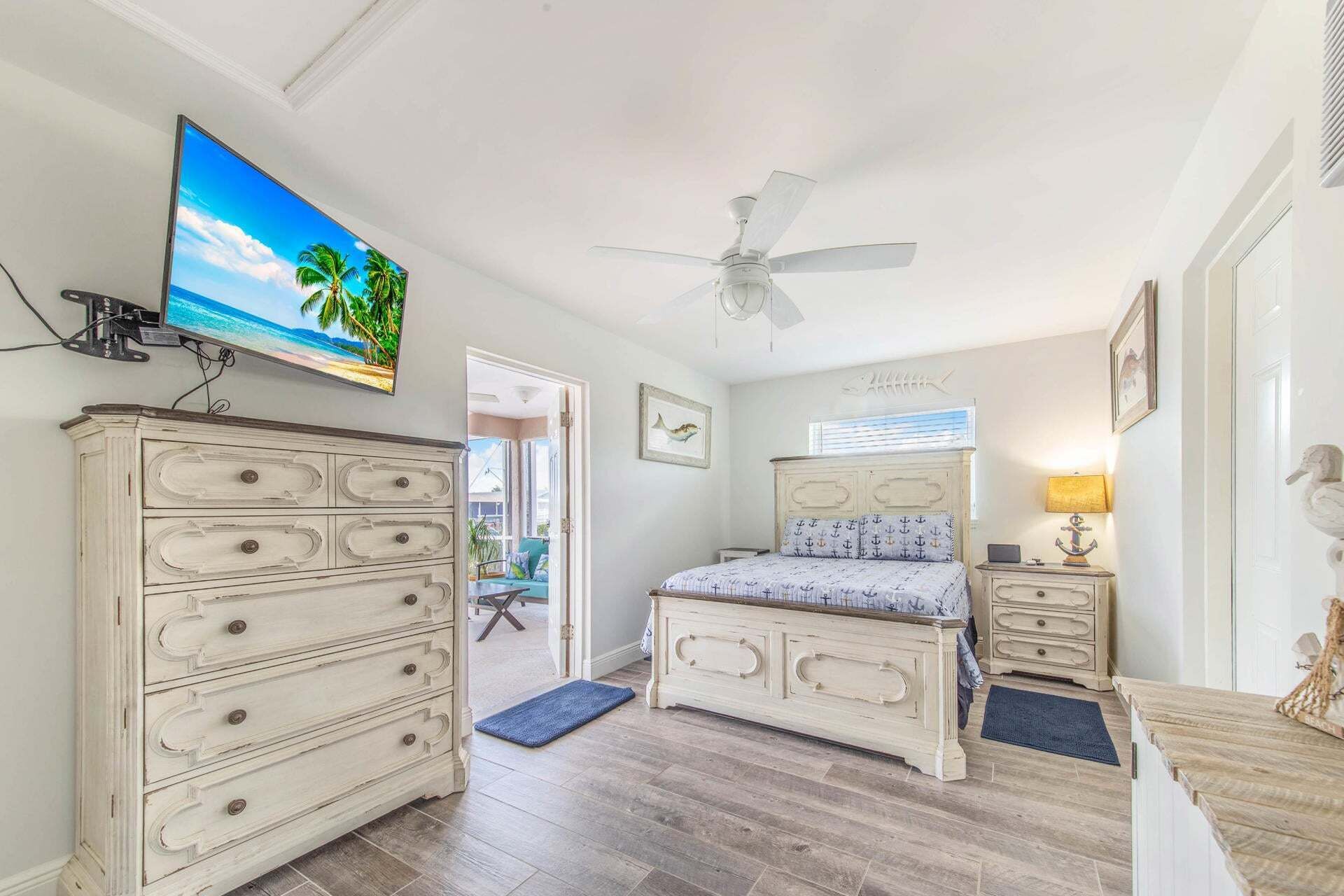 A bedroom with a bed, dresser, television, ceiling fan, and artwork.