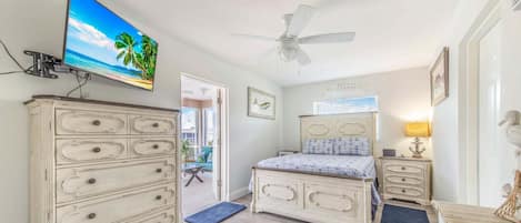 A bedroom with a bed, dresser, television, ceiling fan, and artwork.