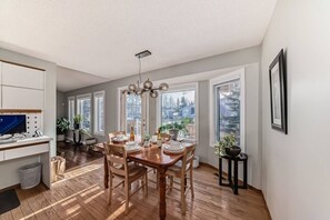 A dining area with a wooden table, chairs, and a chandelier. There are windows with views of trees and houses. - Luxury home in Calgary NW (Calgary)