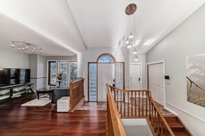 A spacious living area with a wooden staircase, a flat-screen TV, and a large window. - Luxury home in Calgary NW (Calgary)