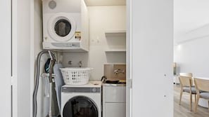 A compact laundry area with a front-loading washer and dryer, a sink, and a small table with chairs. - Azure 25 - Wake up to the Ocean (The Entrance)