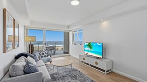 A modern living room with a large TV, a sofa, a coffee table, and a view of the beach. - Azure 25 - Wake up to the Ocean (The Entrance)