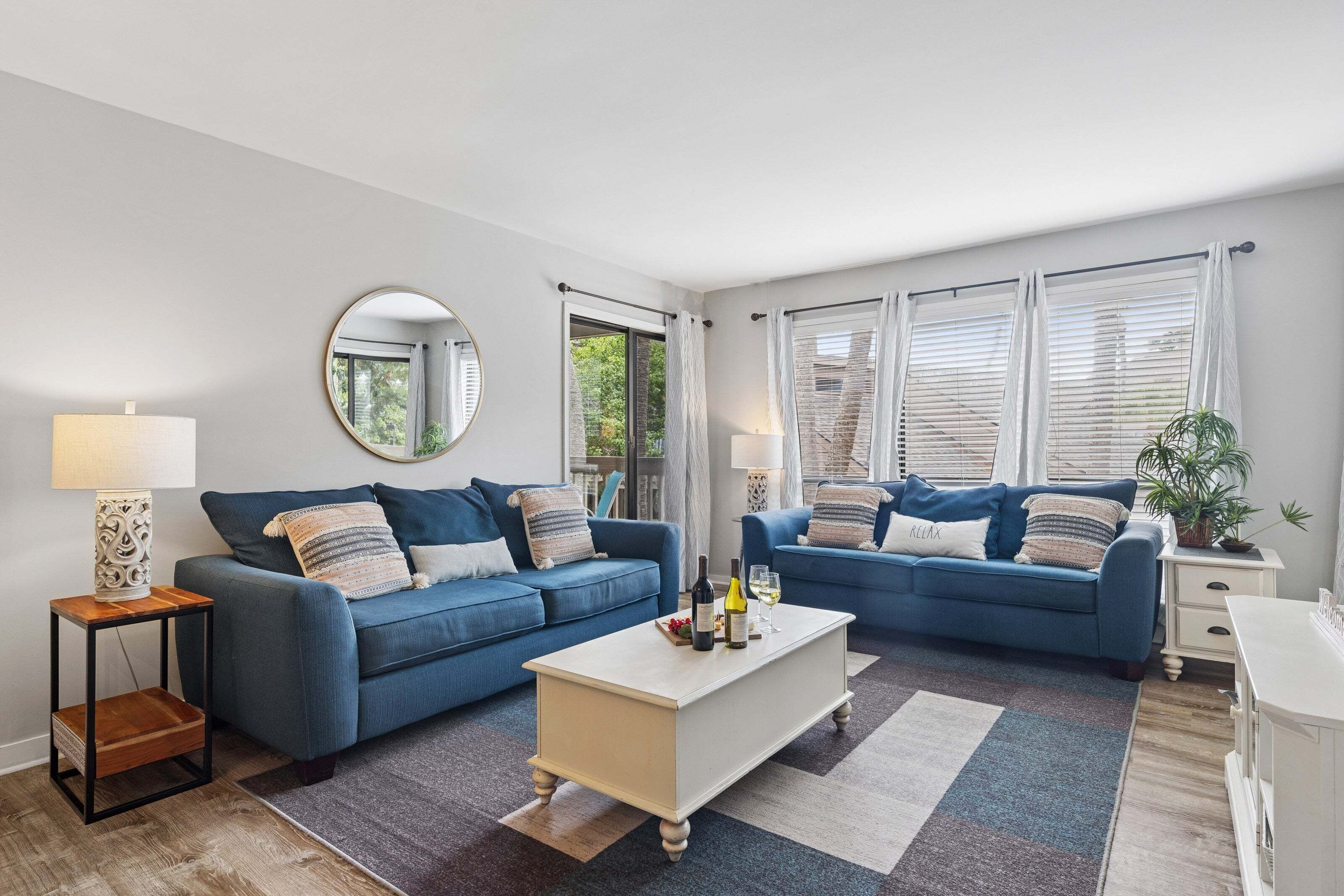 A modern living room with two blue sofas, a coffee table, a round mirror, and a side table with a lamp.