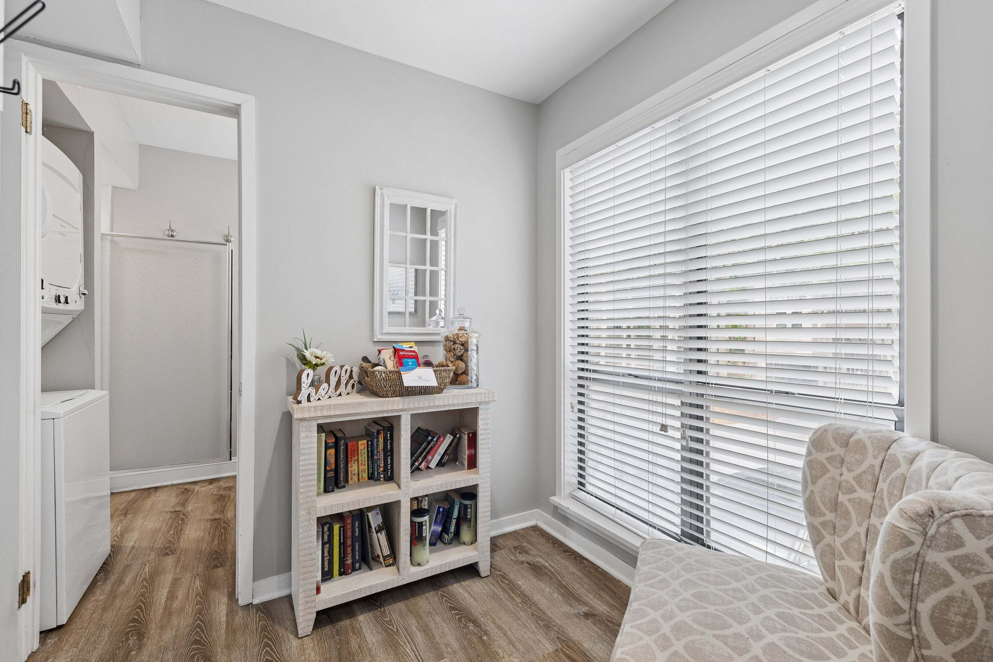 A room with a bookshelf, a window with blinds, and a patterned chair.