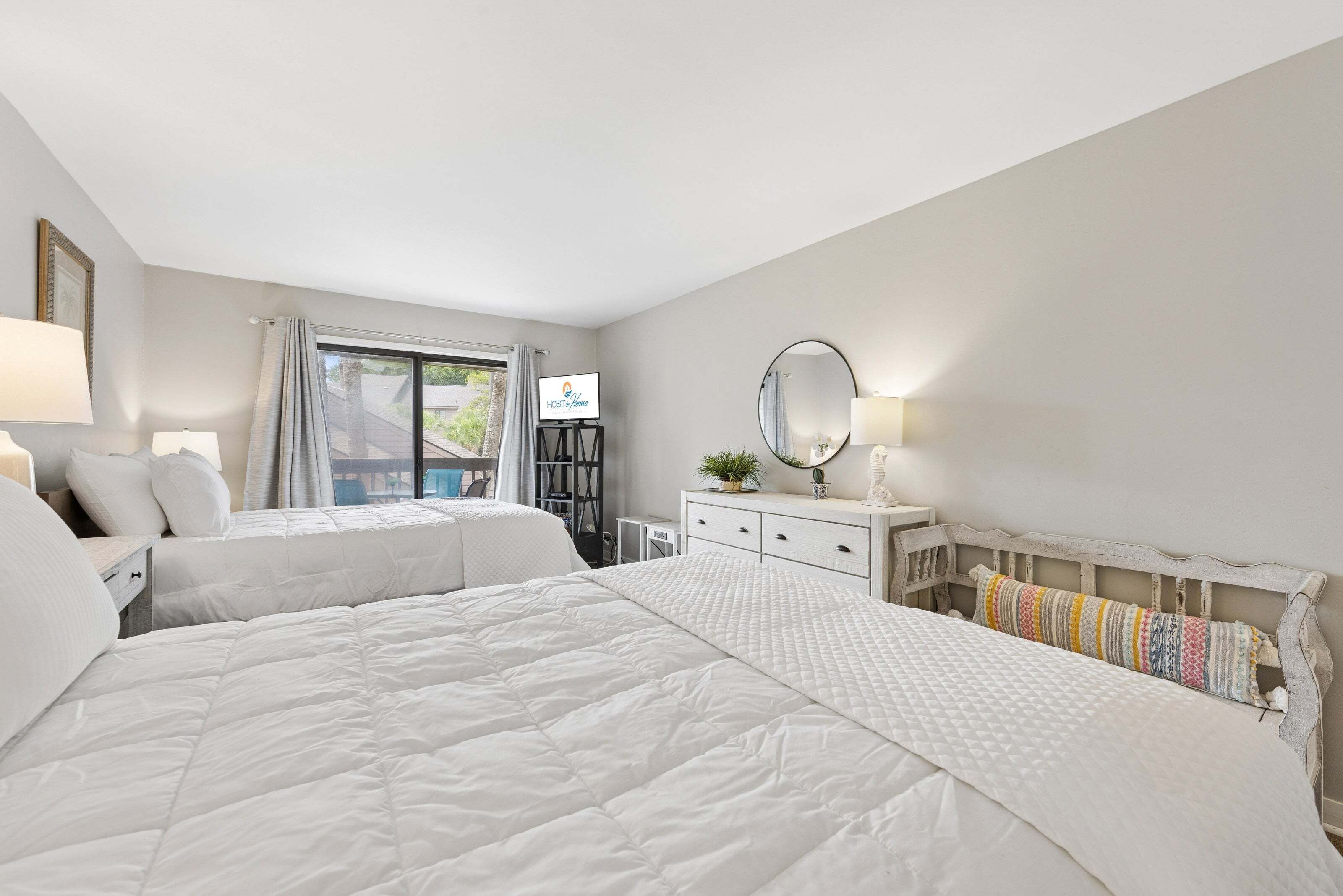 A hotel room with two beds, a desk, a dresser, a mirror, and a television.