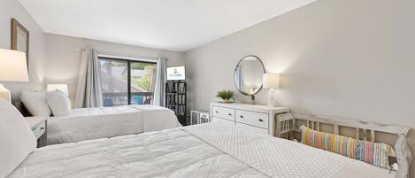 A hotel room with two beds, a desk, a dresser, a mirror, and a television.