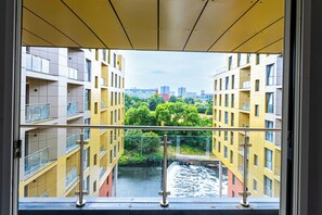 Uitzicht door een raam op een geel gebouw met balkons, met zicht op een rivier en een stadsgezicht.