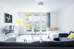 Ein modernes Wohnzimmer mit einer Couch, einem Couchtisch, einem Fernseher und einem großen Fenster mit Blick auf Gebäude.