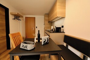 A compact kitchen with a dining area, a wooden chair, a small table, and a bottle of wine. - The Art of Alpine Living, Wallis 1097 (Wallis)