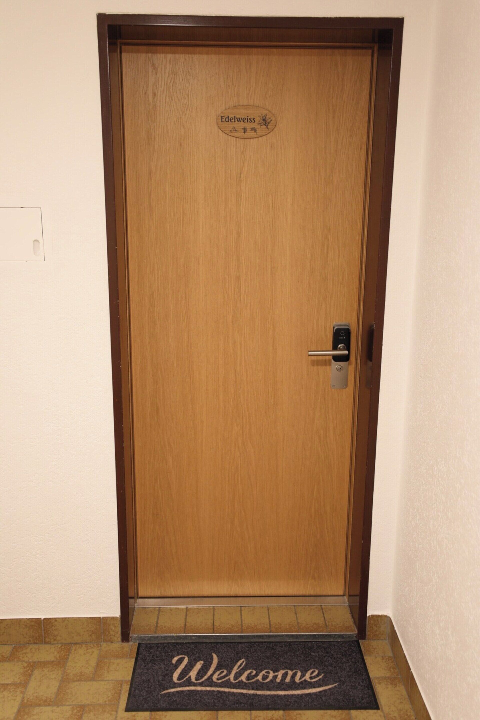 A wooden door with a 'Welcome' mat at the entrance.