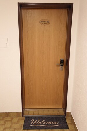 A wooden door with a 'Welcome' mat at the entrance. - Mornings & Refined Alpine Living 1098 (Wallis)