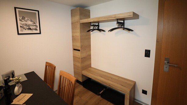 Ein Zimmer mit einem Holzesstisch, Stühlen, einer Bank, einem Kleiderständer und einer Tür.