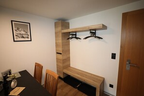 Ein Zimmer mit einem Holzesstisch, Stühlen, einer Bank, einem Kleiderständer und einer Tür.