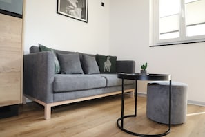 Uma sala de estar moderna com um sofá cinza, uma mesa redonda pequena e um banquinho cinza.