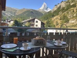 Ein Balkon mit einem Tisch für zwei Personen, einem Korb mit Croissants und einem Glas Orangensaft.