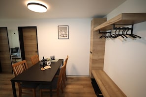 A dining area with a wooden table and chairs, a framed picture on the wall, and a coat rack against the wall. - Alpine Calm with Unforgettable Views 1099 (Wallis)