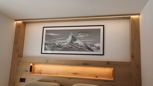 Ein Schlafzimmer mit hölzernem Kopfteil, einem gerahmten Bild von einem Berg und einer eingebauten Ablage.