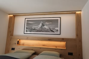 A bedroom with a wooden headboard, a framed picture of a mountain, and a built-in shelf. - Alpine Calm with Unforgettable Views 1099 (Wallis)