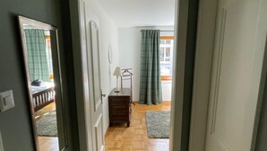 Un pasillo que conduce a una habitación con piso de madera, un espejo y una puerta.