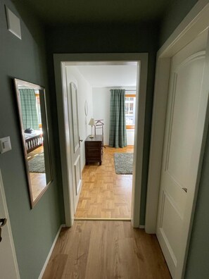 Ein Flur, der zu einem Zimmer mit Holzboden, einem Spiegel und einer Tür führt.