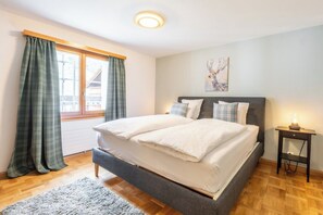 Ein Schlafzimmer mit Bett, Nachttisch, einem Fenster mit Vorhängen und einem Bild an der Wand.
