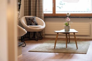 A room with a round armchair, a small table with a potted plant, and a window with blinds. - A Luxurious Retreat Above Zermatt 1100 (Wallis)
