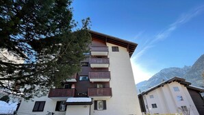 Un edificio de varios pisos con balcones, suelo cubierto de nieve y bicicletas estacionadas afuera.