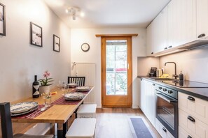 Eine kompakte Küche mit Essbereich, ausgestattet mit einem Holztisch, Stühlen, einer Uhr und einem Fenster mit Blick.
